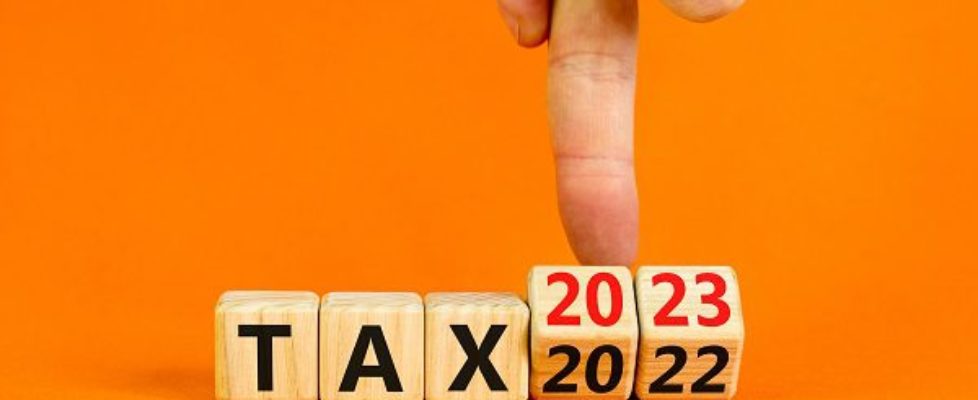 2023 tax new year symbol. Businessman turns a wooden cube and changes words Tax 2022 to Tax 2023. Beautiful orange table orange background, copy space. Business 2023 tax new year concept.